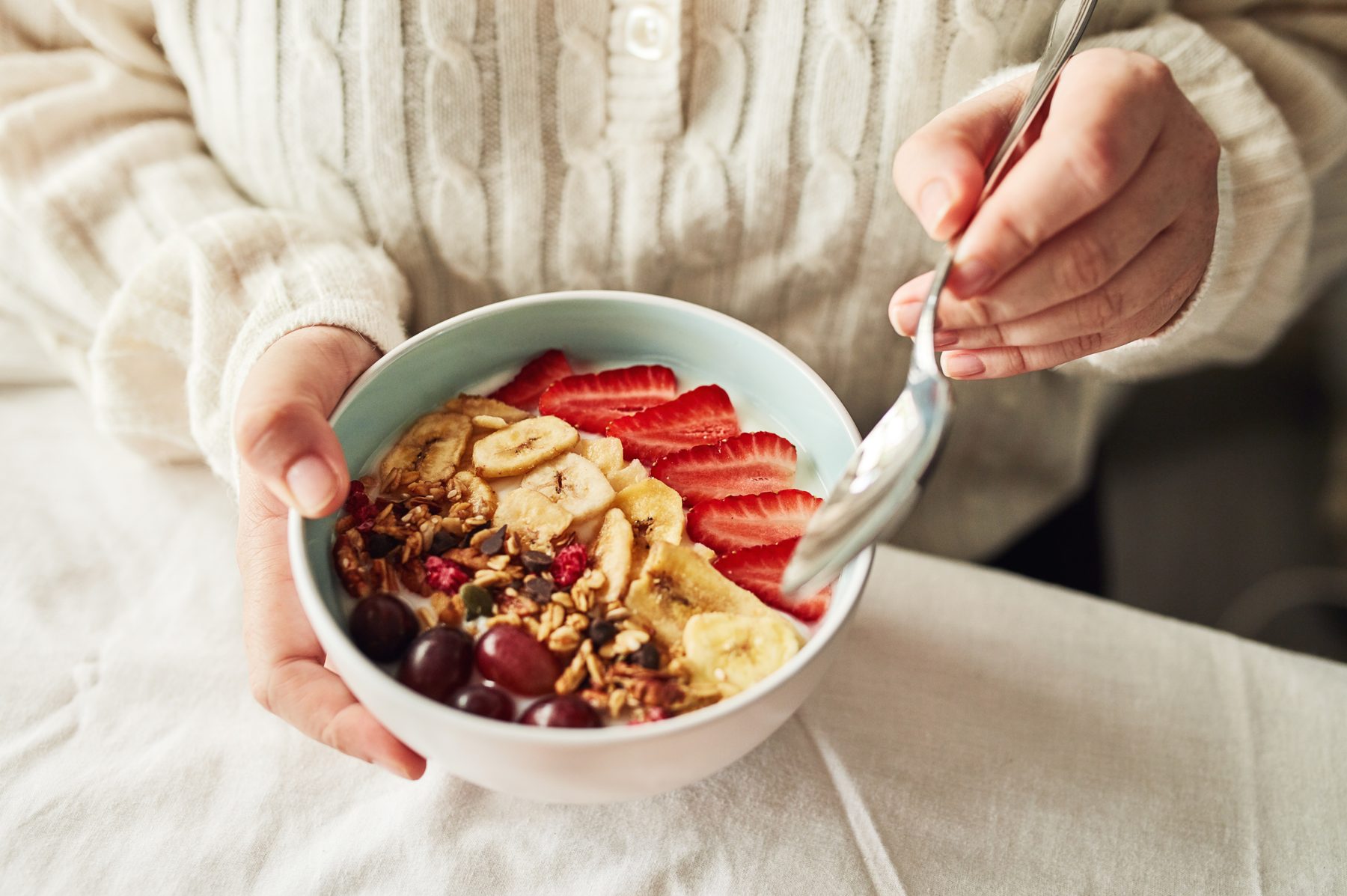 A bowl of yoghurt with granola, banana, strawberries and grapes