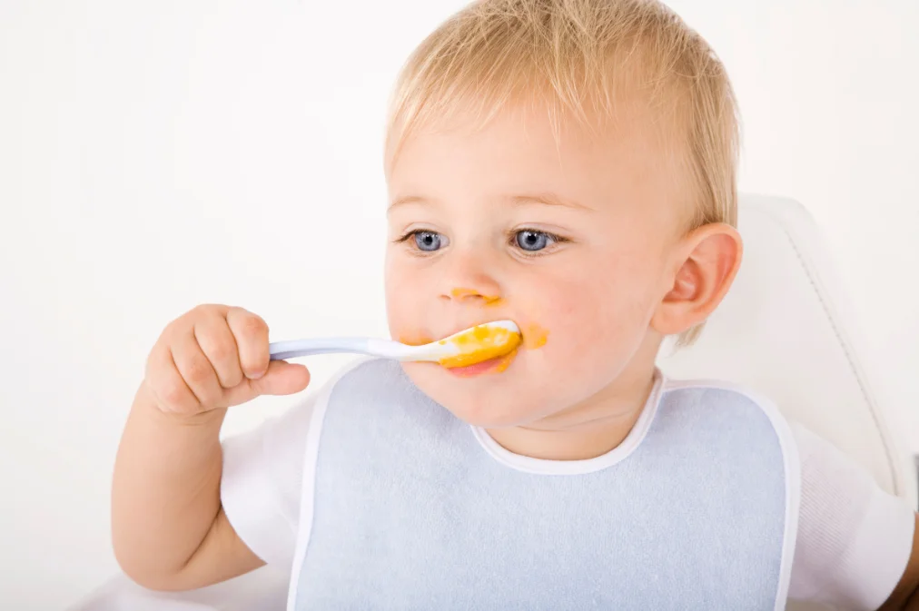 A toddler feeding themselves with a spoon